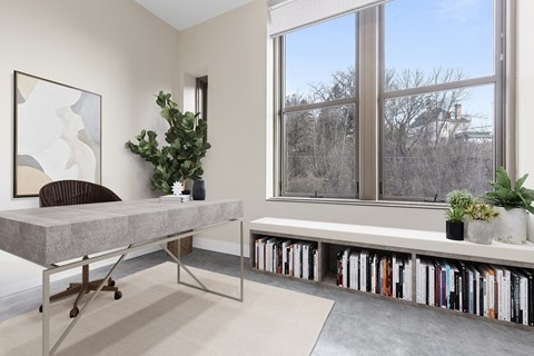 a home office with a large window and a table with bookshelves