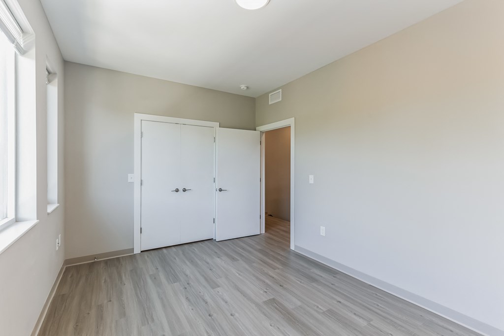 a bedroom with white walls and wood flooring and a door to a closet