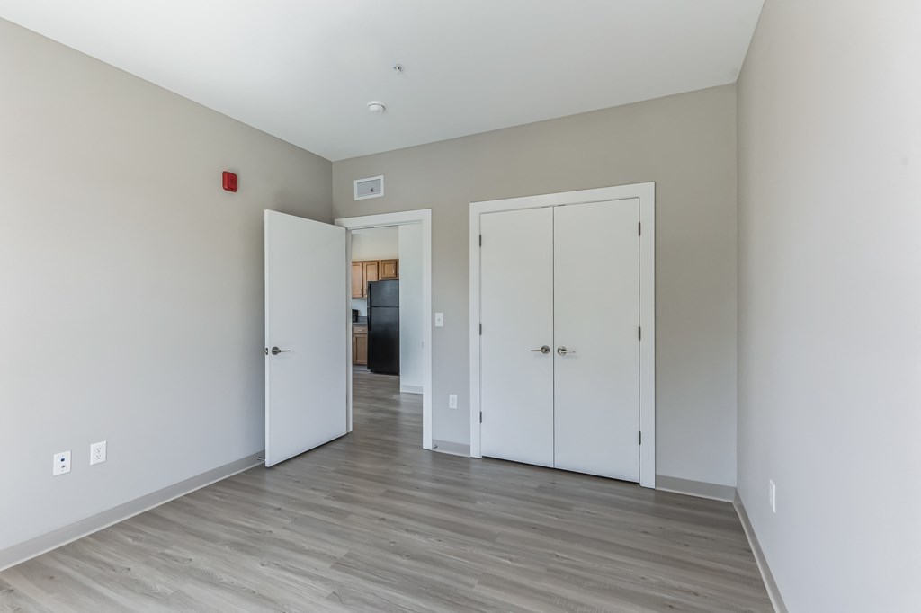 a bedroom with white walls and wood flooring and two closets