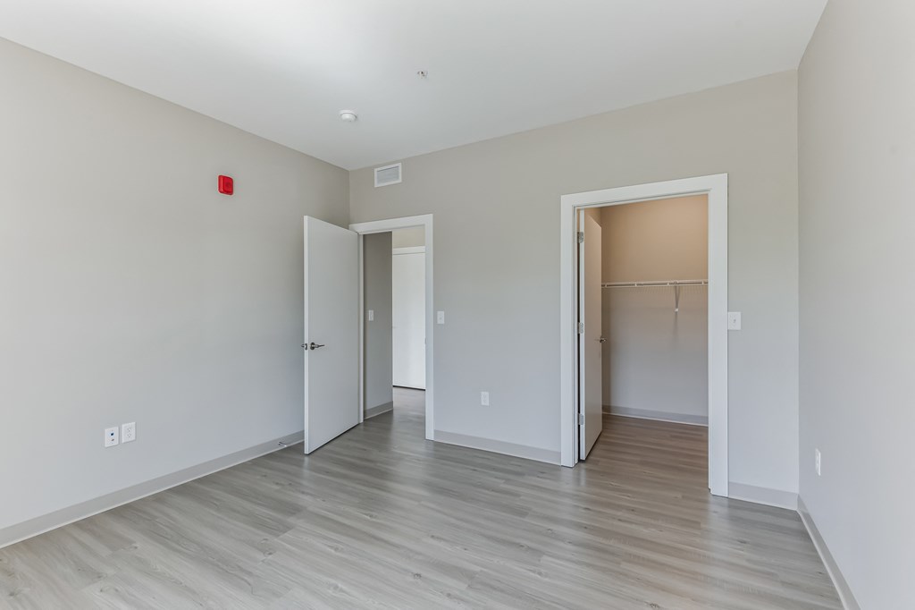 a bedroom with white walls and wood flooring and a closet