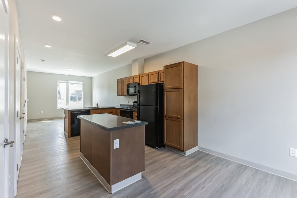 an empty apartment with a kitchen and a black refrigerator