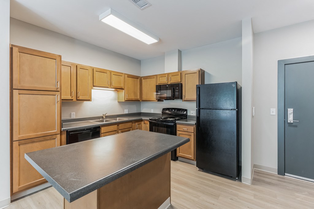 an empty kitchen with wooden cabinets and a black refrigerator