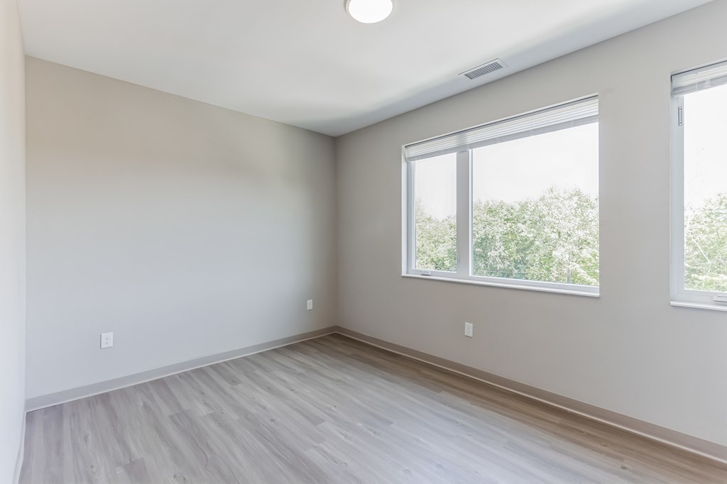 an empty room with wood floors and two windows