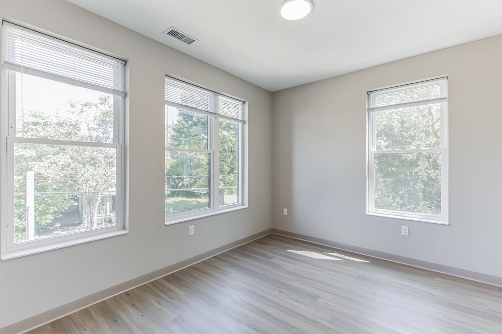 an empty bedroom with three windows and a wood floor