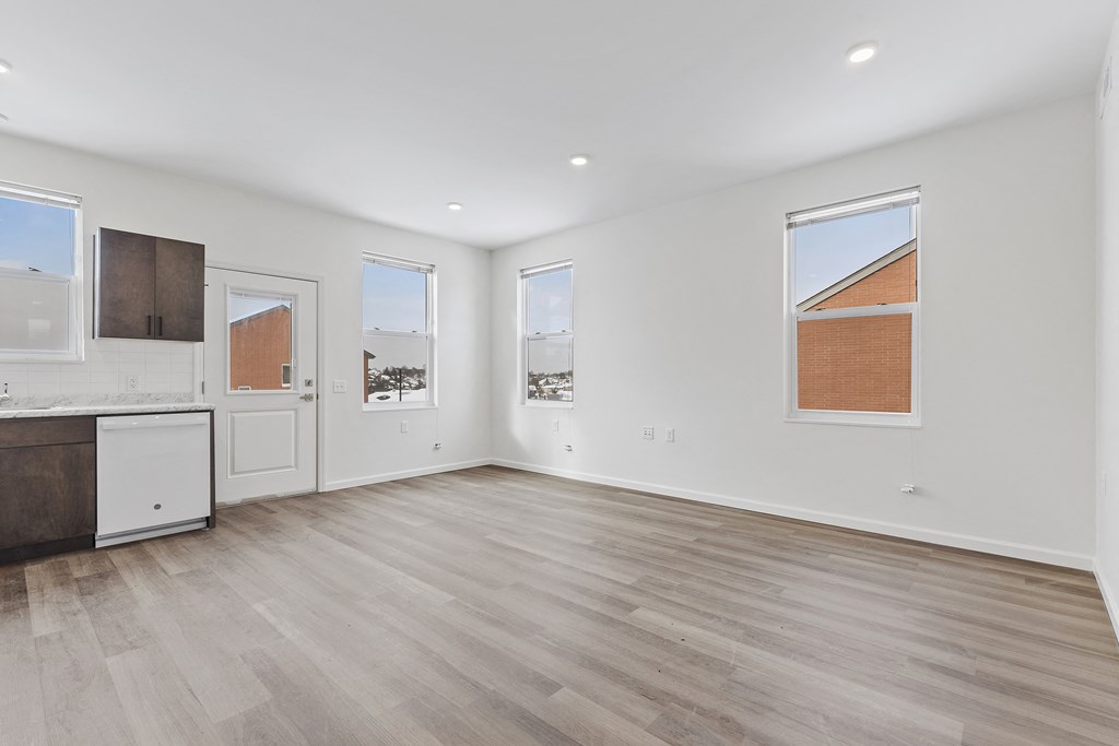 a living room with white walls and wood floors and a kitchen