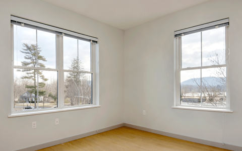 Two windows in a room with wooden floors and white walls.
