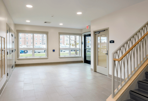 A hallway with a staircase on the right and a door at the end.
