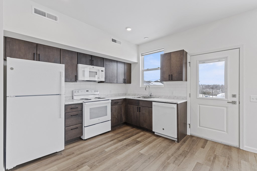 an empty kitchen with white appliances and wooden floors