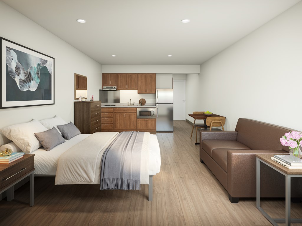 A modern bedroom with a large bed and a kitchen area in the background.