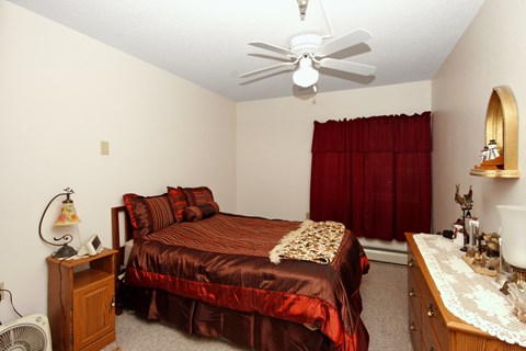 A bedroom with a bed, dresser, and ceiling fan.