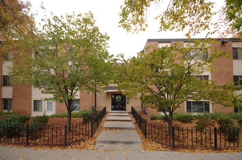 A brick building with a black fence and trees in front.