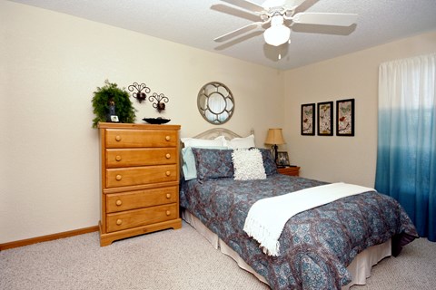 A bedroom with a bed, dresser, and a ceiling fan.