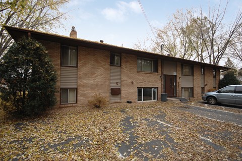 A house with a brown brick exterior and a grey roof with a car parked in front.