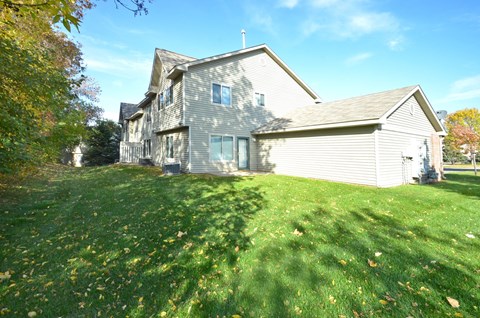 A house with a grey siding and a white roof is surrounded by a grassy lawn with fallen leaves.