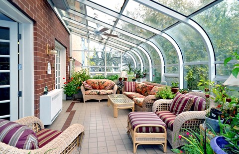 A sunroom with a glass ceiling and walls, furnished with wicker chairs and tables.