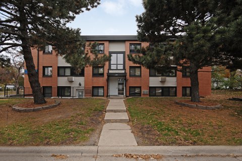 A red brick apartment building with a tree in front.