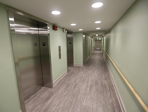 A long hallway with elevators on the left and a yellow line on the right.