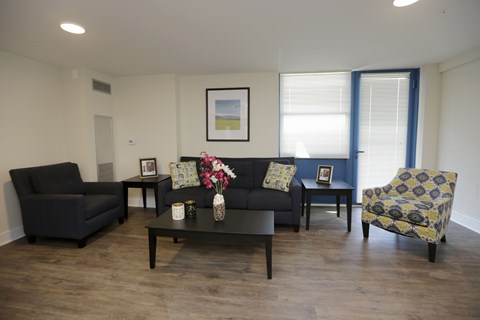 A living room with a black couch, a black armchair, a coffee table, and a yellow and blue patterned chair.