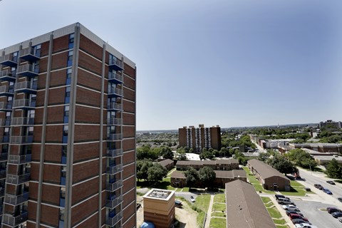 A tall brick building with many windows is in the foreground of a cityscape.