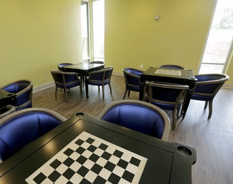 A room with a chessboard in the foreground and several chairs and tables.