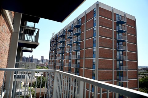 A tall red brick building with balconies and a view of the city in the distance.