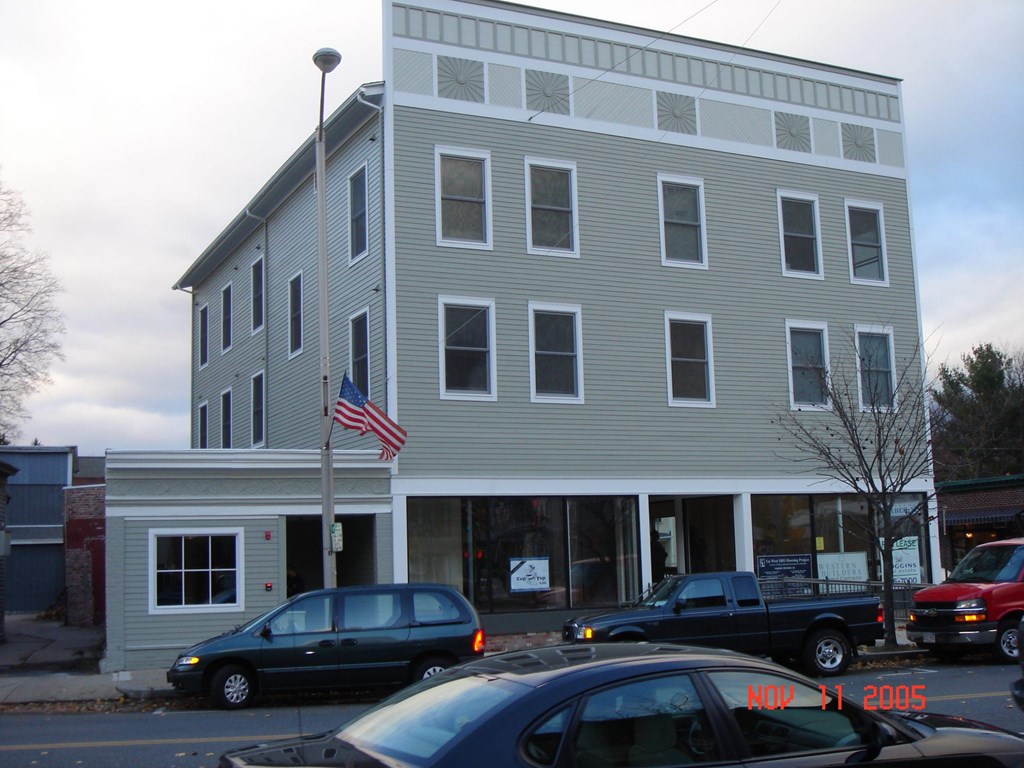 A grey building with a flag on top and cars parked in front.