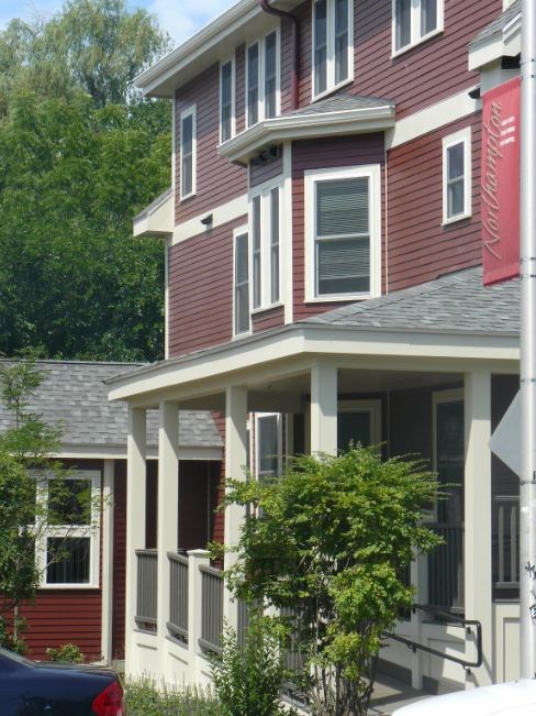 A red house with a white porch and a car parked in front.