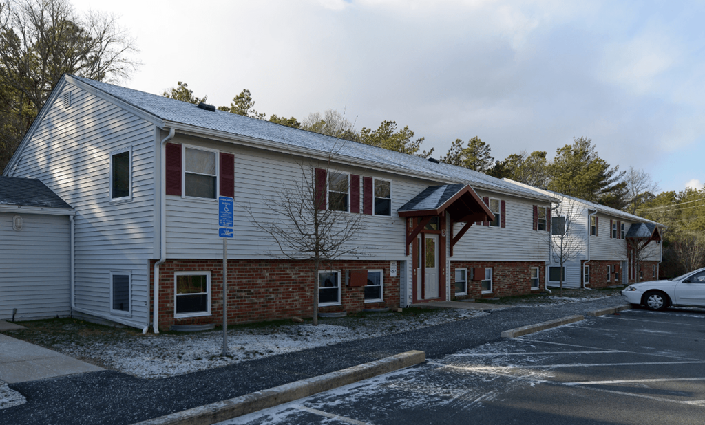 A building with a red brick wall and a white siding with a car parked in front.