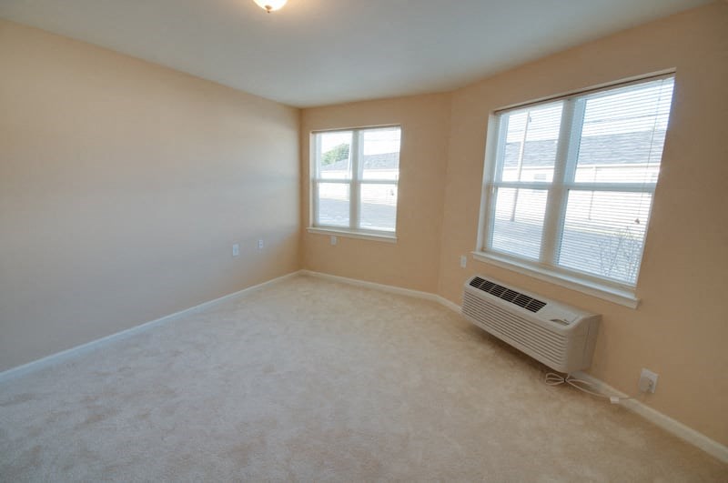an empty living room with a heater and two windows