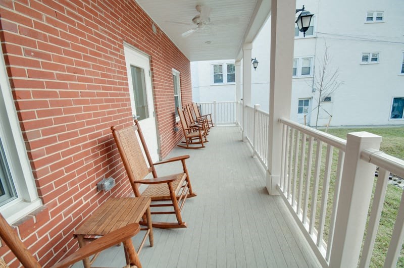 a porch with wooden chairs and a brick wall