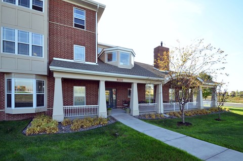 A brick building with a white porch and a tree in front.