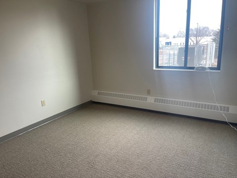 A carpeted room with a window and a wall-mounted air conditioner.