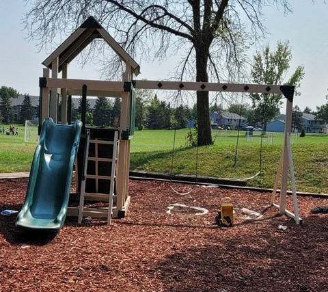 A playground with a green slide and a wooden swing set.