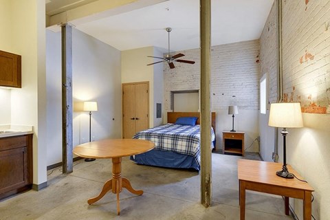 A bedroom with a bed, a table, and a ceiling fan.