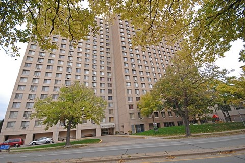 A tall building with many windows is surrounded by trees.