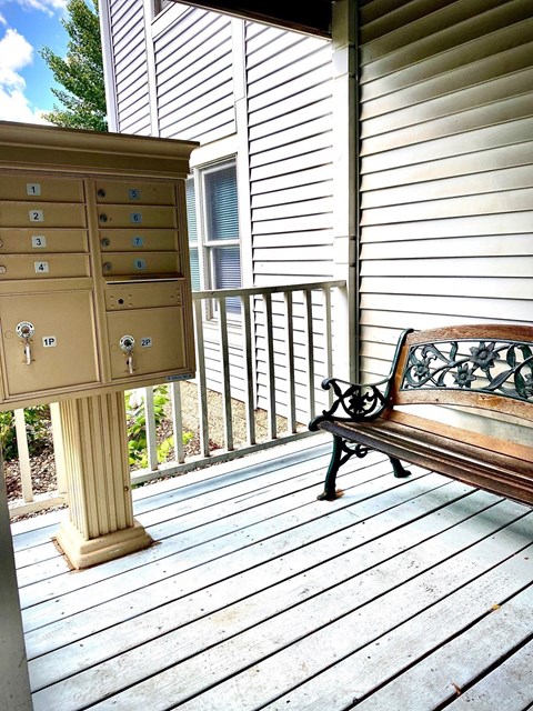A bench sits on a porch next to a mailbox.