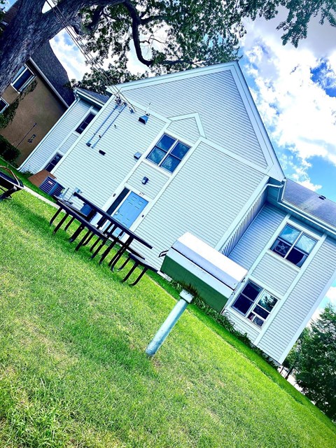 A house with a blue siding and a white roof with a tree in the background.