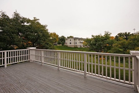 A wooden deck with a white railing overlooks a green lawn and a house.