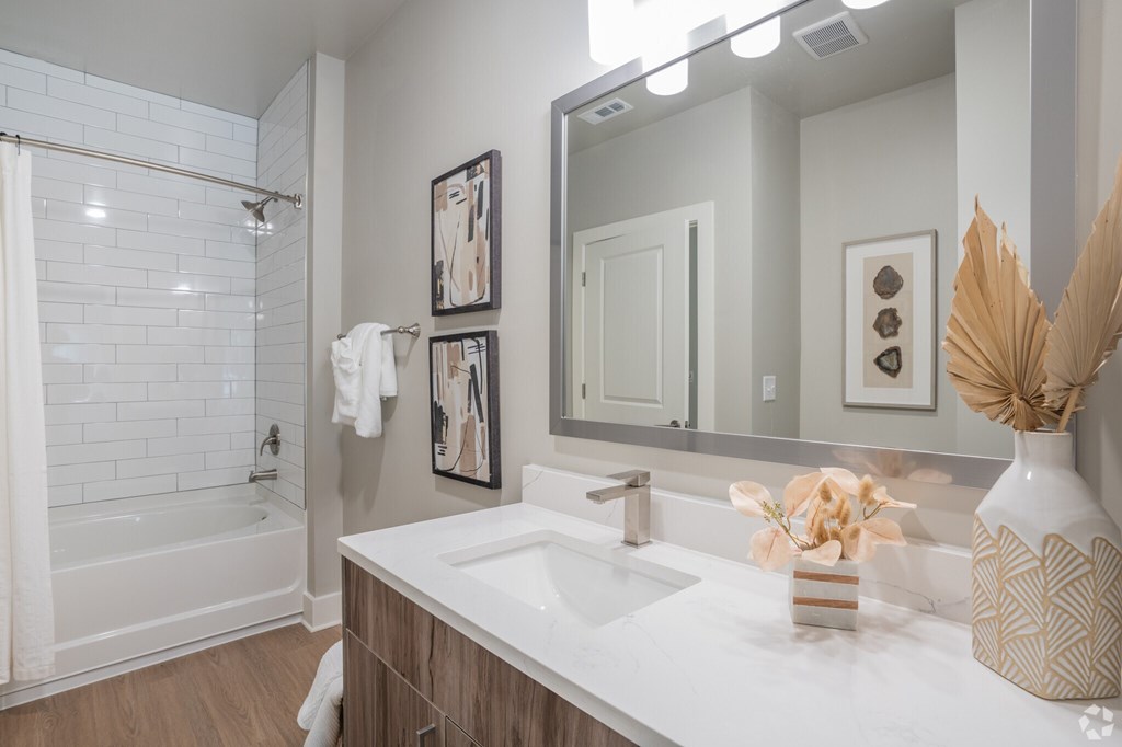 A white sink in a bathroom with a white tub and a mirror.at The Delaney at East Park Apartments, Kennesaw, GA, 30144