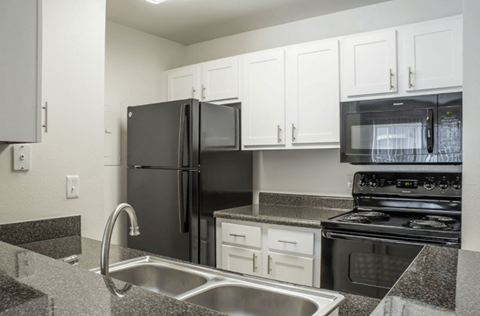 A black refrigerator is in a kitchen with granite countertops and stainless steel appliances.