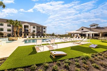 a pool and lounge chairs in a yard with apartments in the background at The Parker Austin, Pflugerville, TX