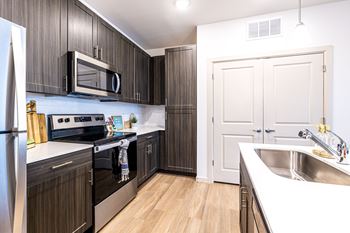 a kitchen with dark wood cabinets and stainless steel appliances and a sink at The Parker Austin, Pflugerville