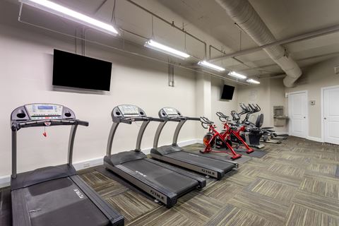 a gym with treadmills and bikes and a tv on the wall