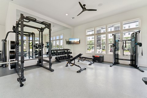 A spacious gym with a variety of equipment including a squat rack, bench, and weights at The Hendry Apartments, Fort Myers, FL