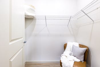 a walk in closet with a chair and a pillow and a white wall with aat The Parker Austin, Pflugerville, TX