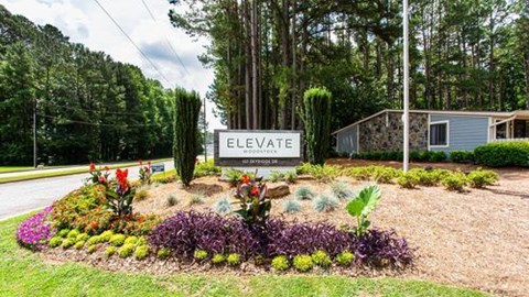 A sign that says "ELEVATE" stands in front of a flower bed.