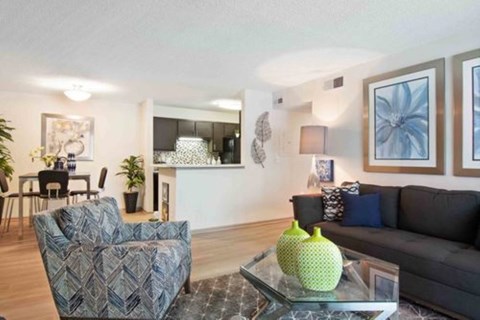 A living room with a grey couch, a patterned armchair, and a glass coffee table with a green vase on it.