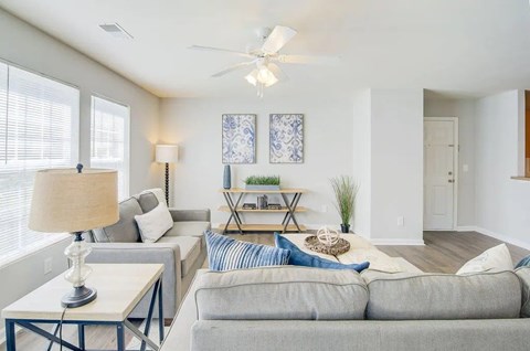 A living room with a grey couch, a table with a lamp, and a ceiling fan.