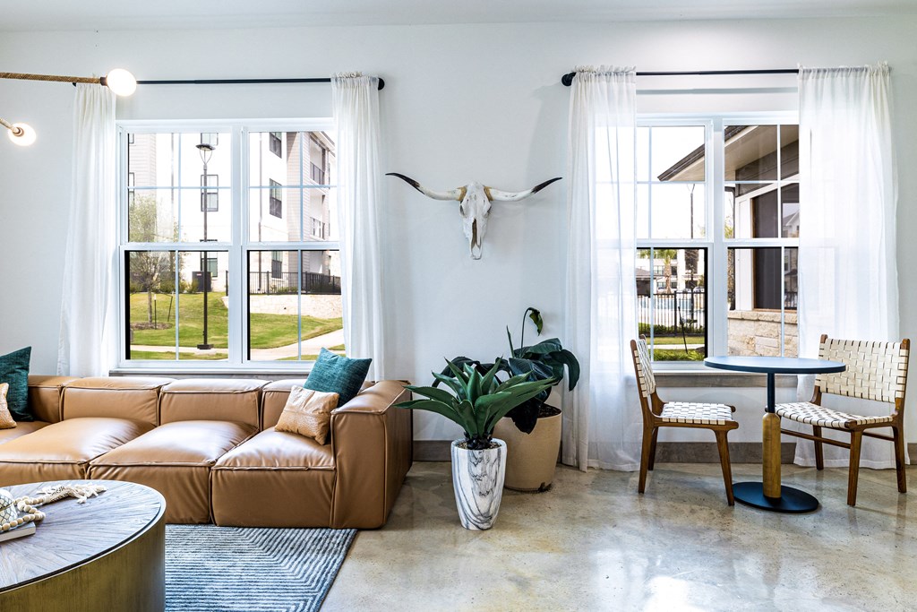 a living room with a leather couch and a table and windows at The Parker Austin, Pflugerville, Texas