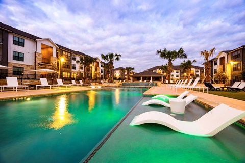 a large pool with a lounge chair in the water at an apartment complex